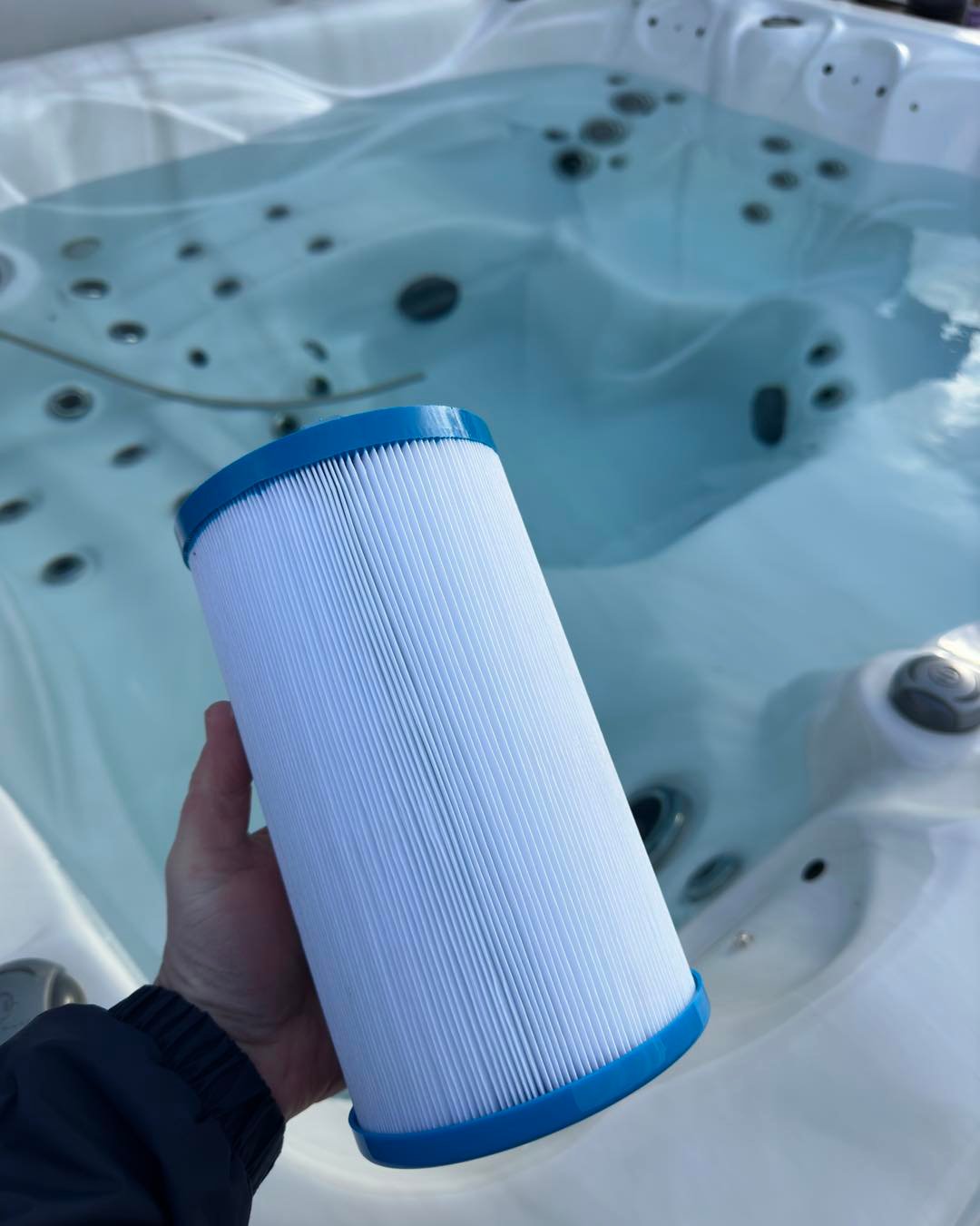 A pristine, chemically cleaned hot tub filter held against a clear spa to demonstrate filtration efficiency.